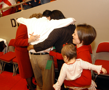 Head Coach Mark Campbell prays with his coaching staff Katie Woodruff and Tonya Tuggles.  Campbell's wife and daughter wait to celebrate after Union's title win in the NAIA National Tournament. - Photo by Morris Abernathy