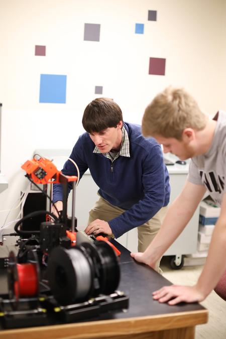 Georg Pingen, associate professor of engineering, works with Nathan Cole, engineering major, on a 3D printer.  - Photo by Kristi McMurry Woody