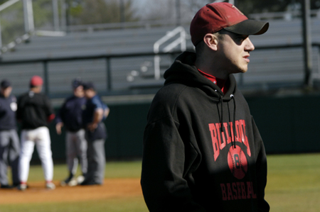 Injured senior, Jason Johnson waits for the game to start as the coaches and umpires meet at homeplate. - Photo by Kathleen Murray