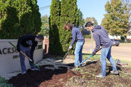 Professor Matthew Albanese works with students on clearing out a flower bed at West Jackson Baptist Church for Campus and Community Day. - Photo by Karley Hathcock