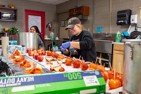 SAC Member Joelle Cruver makes candy apples at the Boys & Girls Club in Humboldt during Campus and Community Day. - Photo by Lyla Dietz