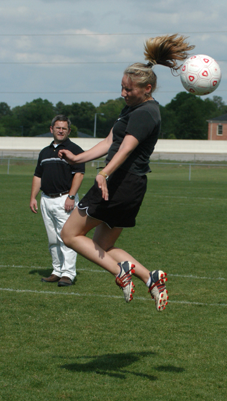 Megan Okerson heads a ball during spring drills with Head Coach Brandon Boylan looking on in the background. - Photo by Heather Phillips
