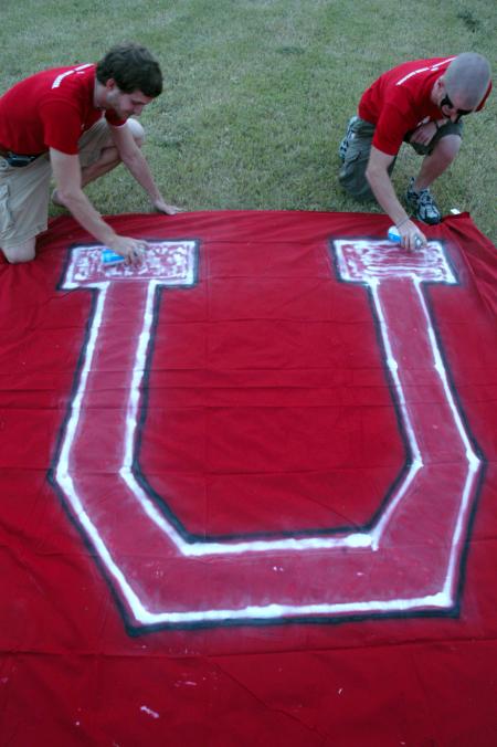 Ronald Long and Mike Evans prep the U flag with an extra coat of spray paint moments before the pep rally march from Miller Tower to the soccer fields. - Photo by Kyle Kurlick