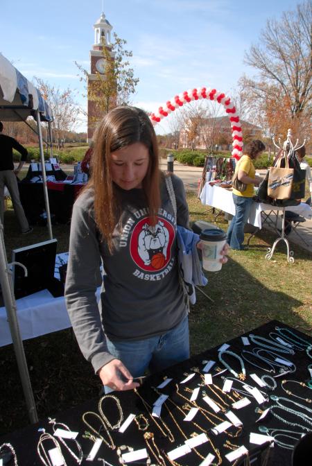 Junior Mary Kinberg, nursing major, looks over some jewelry for sale by alum artists at the Arts in the Park event during Homecoming. - Photo by Morris Abernathy