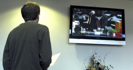 Alum and Enrollment Counselor Brad Spencer watches fall graduation on screen in the lobby at West Jackson Baptist Church. - Photo by Matthew Diggs