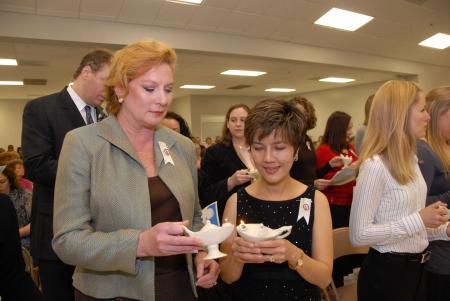 Darcy Brown (left) passes the lamplight to Carmen Cabanero during the nursing pinning ceremony prior to fall graduation. - Photo by Morris Abernathy
