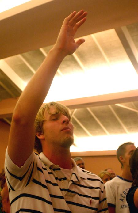 Sophomore Carter Collins raises his hand in praise as he sings along during the family chapel on the first day of orienation. - Photo by Stephanie Schroeder