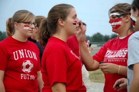 Sophomore Psychology Major April McCulley paints the face of Hunner Coward, sophomore undecided major, as Kayla Clary, sophomore social work major, looks on before a Lady Bulldog soccer match. - Photo by Matt Elia