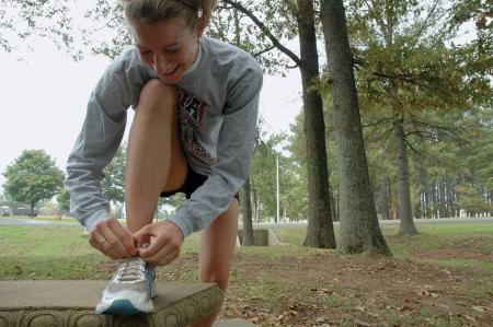 Making sure the laces are tied tightly, Junior Lydia Bond prepares to run a cross country meet on campus.  - Photo by Neisha Fuson